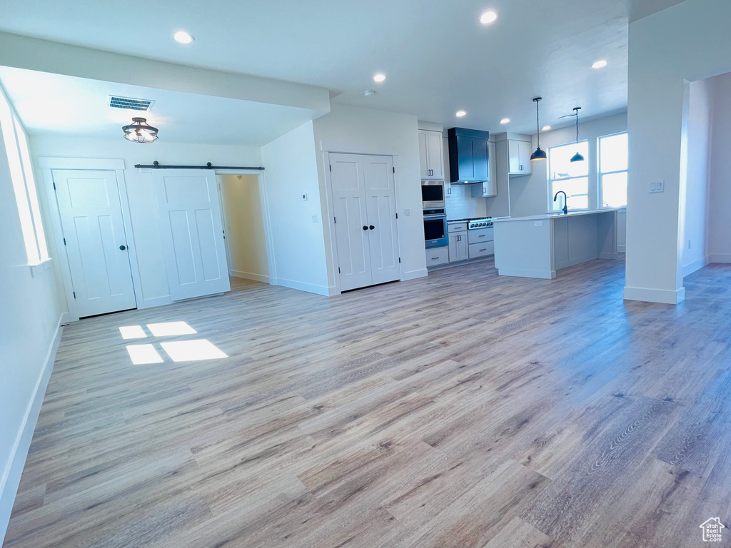 Unfurnished living room featuring baseboards, light wood-style flooring, recessed lighting, a barn door, and a sink
