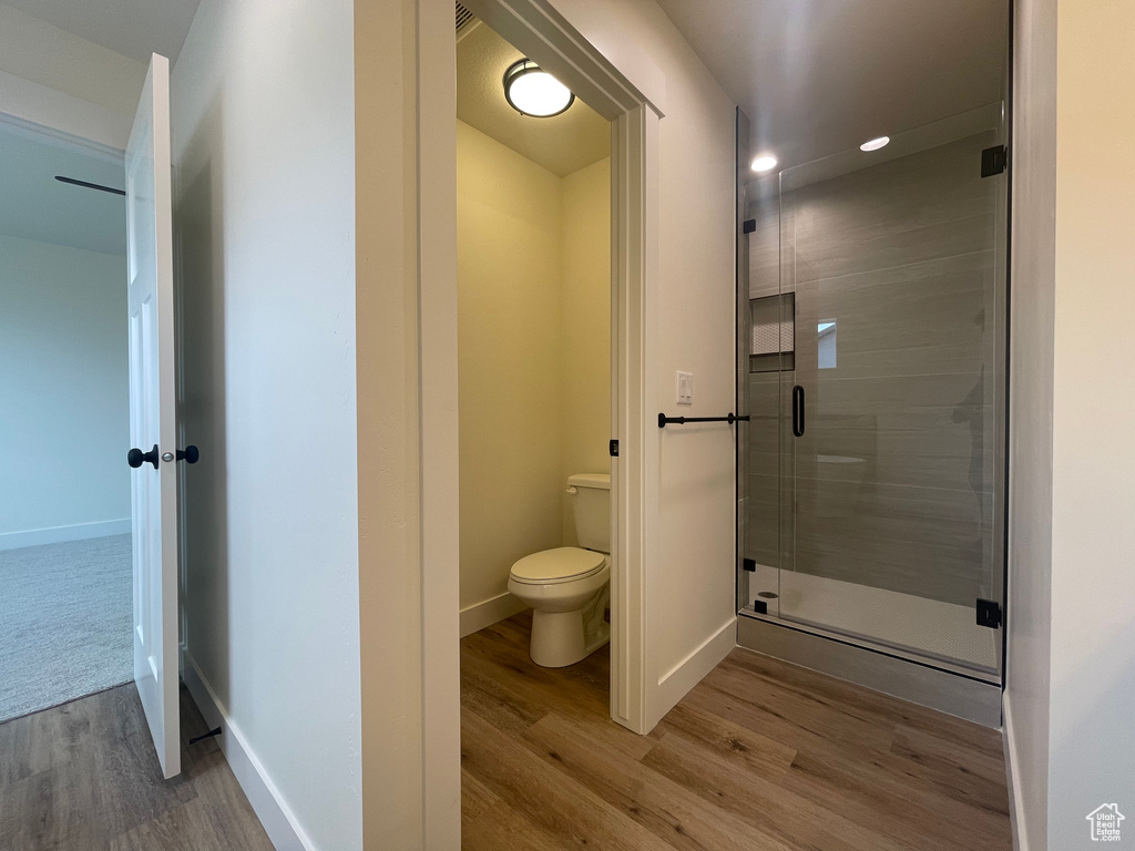 Bathroom with wood finished floors, a stall shower, toilet, baseboards, and recessed lighting