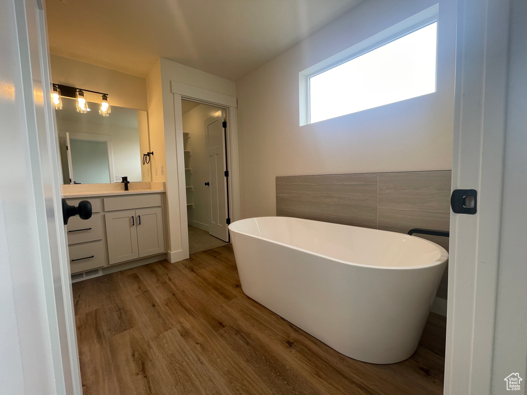 Full bath with wood finished floors, vanity, and a soaking tub