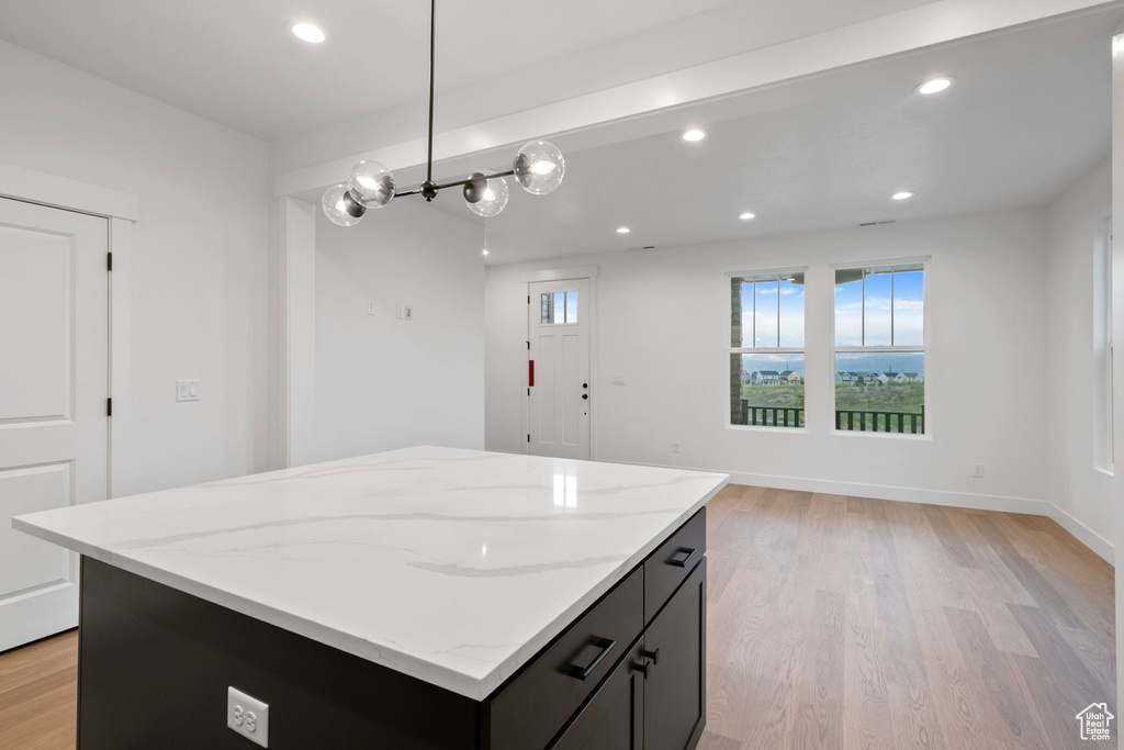 Kitchen with light wood-style flooring, a center island, light stone counters, recessed lighting, and pendant lighting