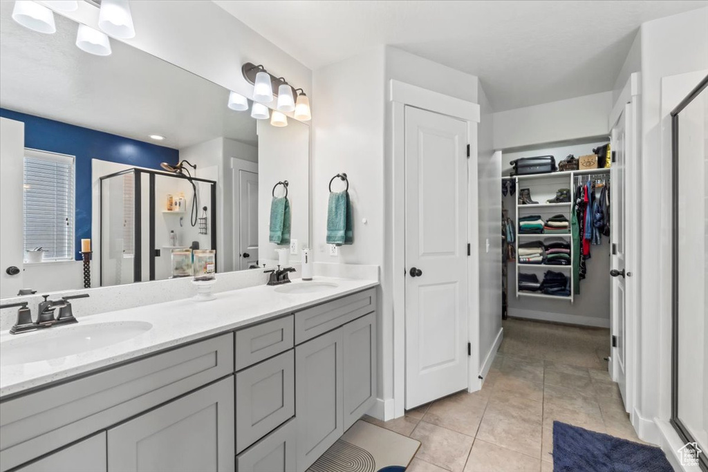 Bathroom featuring a shower stall, double vanity, tile patterned floors, and a spacious closet