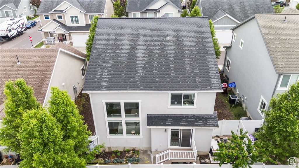 Back of house featuring a shingled roof, a residential view, stucco siding, cooling unit, and fence
