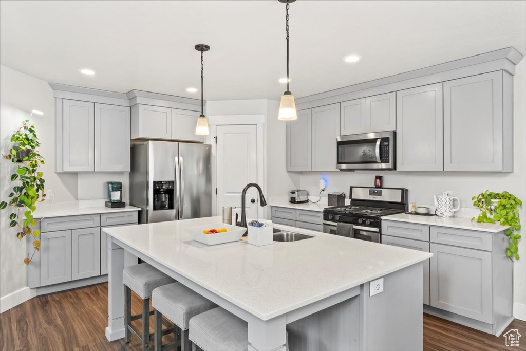 Kitchen featuring stainless steel appliances, a sink, a center island with sink, dark wood finished floors, and a breakfast bar area