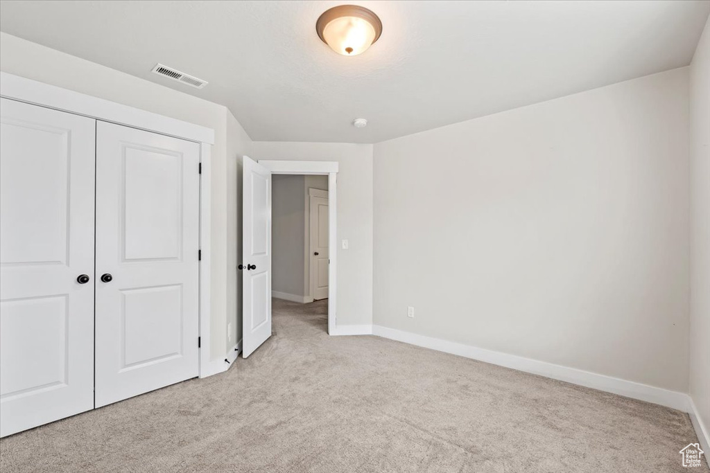 Unfurnished bedroom featuring light colored carpet, baseboards, and a closet
