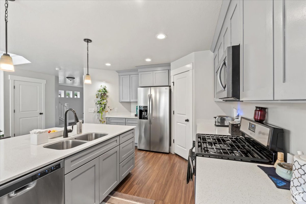 Kitchen with appliances with stainless steel finishes, a sink, gray cabinets, recessed lighting, and decorative light fixtures