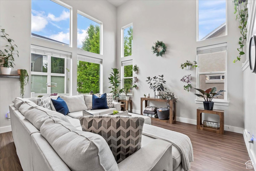 Living area featuring a high ceiling, healthy amount of natural light, wood finished floors, and baseboards