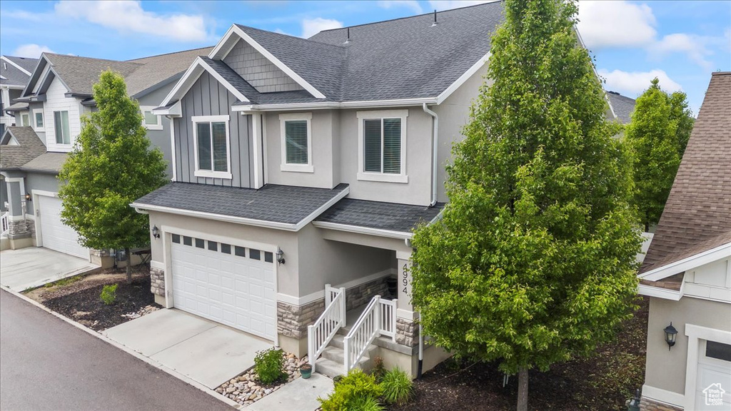 View of front of house with stone siding, roof with shingles, an attached garage, and concrete driveway