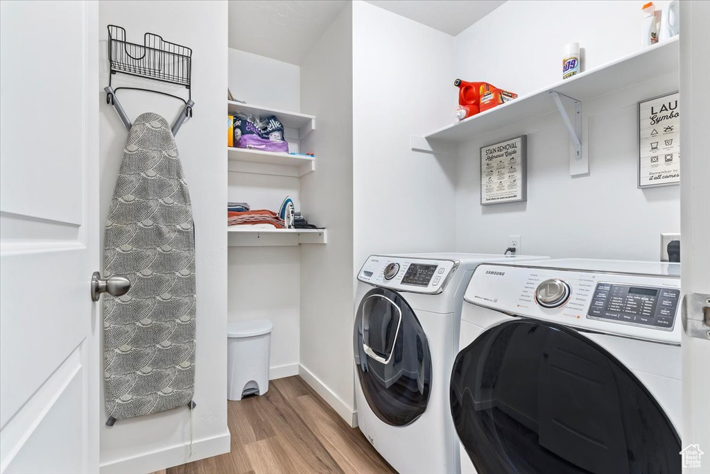 Washroom with washing machine and clothes dryer, wood finished floors, and baseboards