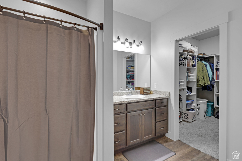 Bathroom with wood finished floors, vanity, a walk in closet, and a shower with curtain