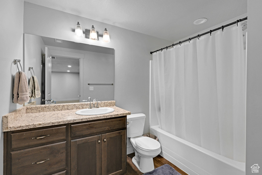 Bathroom with toilet, vanity, wood finished floors, and shower / bath combo with shower curtain