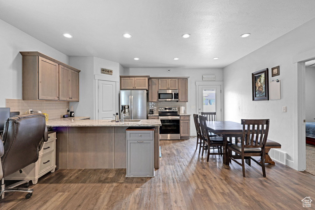 Kitchen with stainless steel appliances, a peninsula, dark wood finished floors, decorative backsplash, and recessed lighting