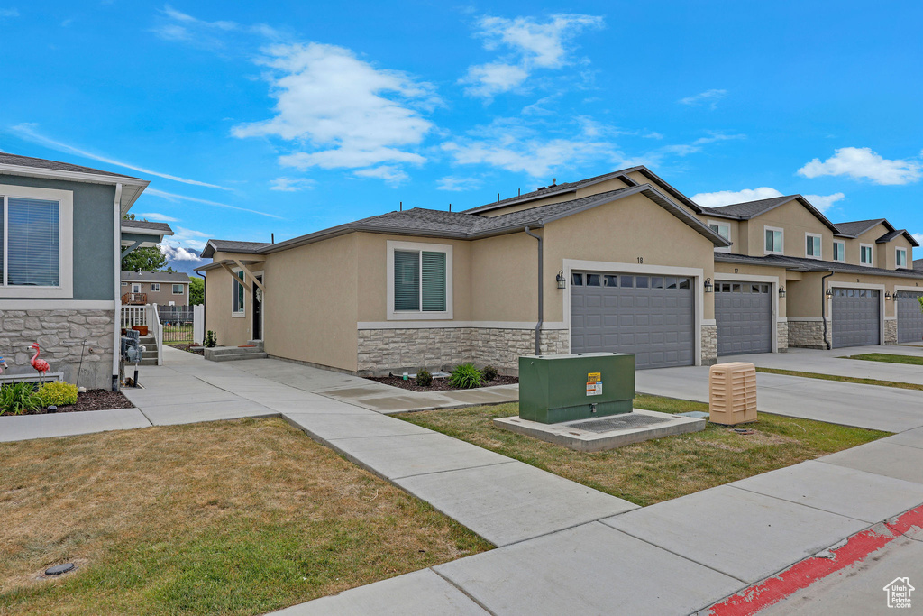 View of front of home with stone siding, stucco siding, concrete driveway, a garage, and a front yard