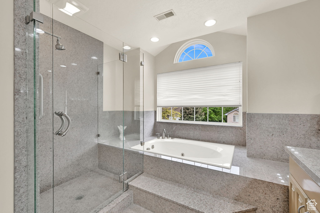 Full bath featuring plenty of natural light, a stall shower, a jetted tub, vaulted ceiling, and vanity