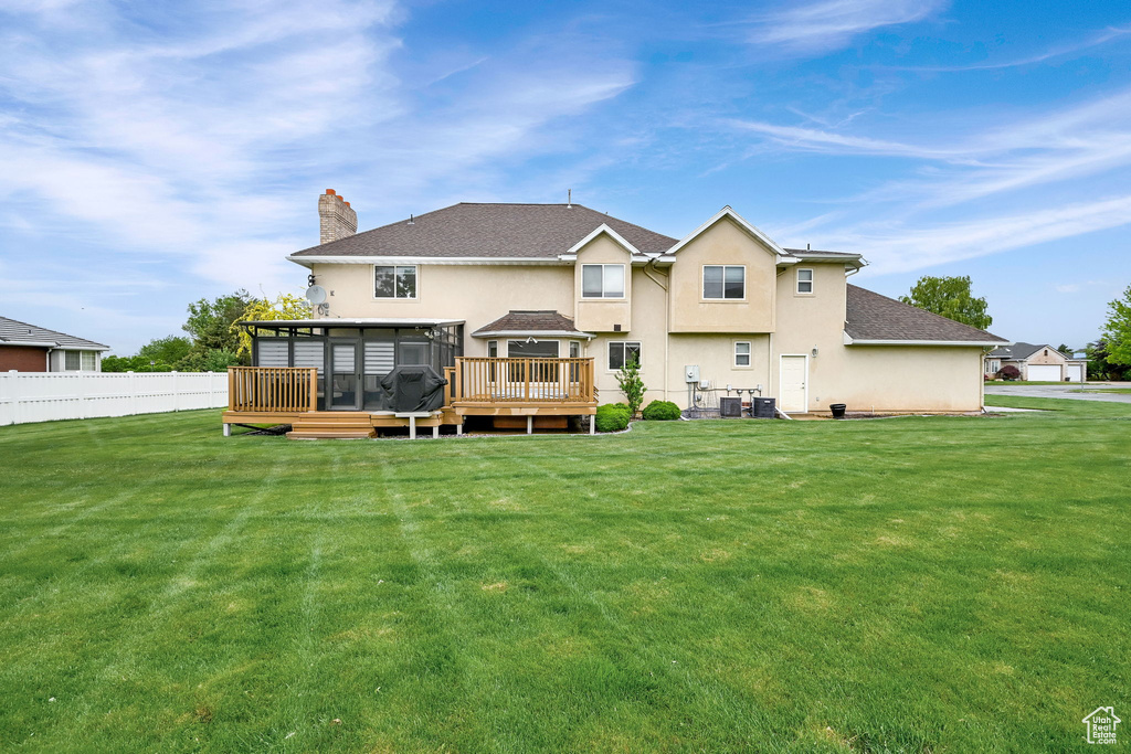 Back of property with a sunroom, a chimney, stucco siding, a wooden deck, and a shingled roof