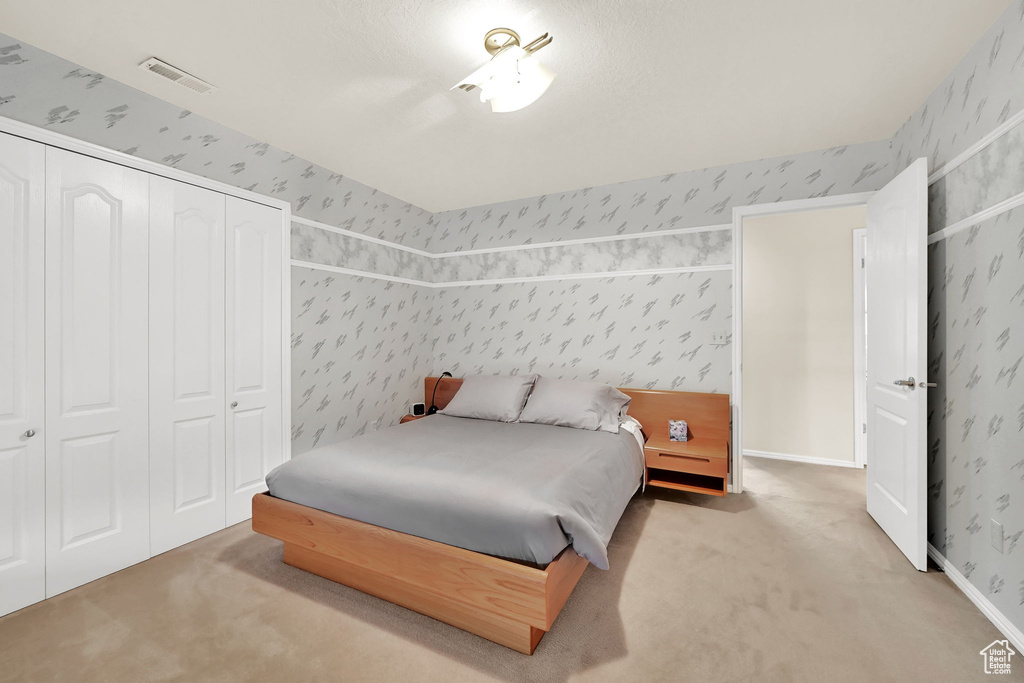 Carpeted bedroom featuring wallpapered walls and a closet