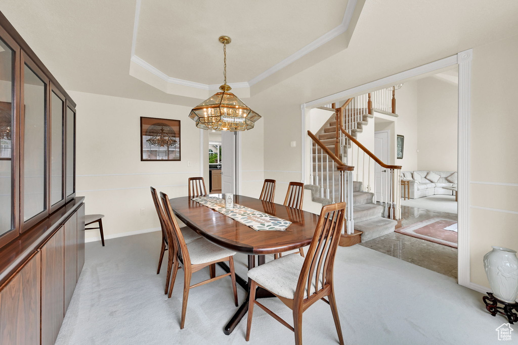Dining area featuring light colored carpet, stairway, a tray ceiling, a chandelier, and crown molding