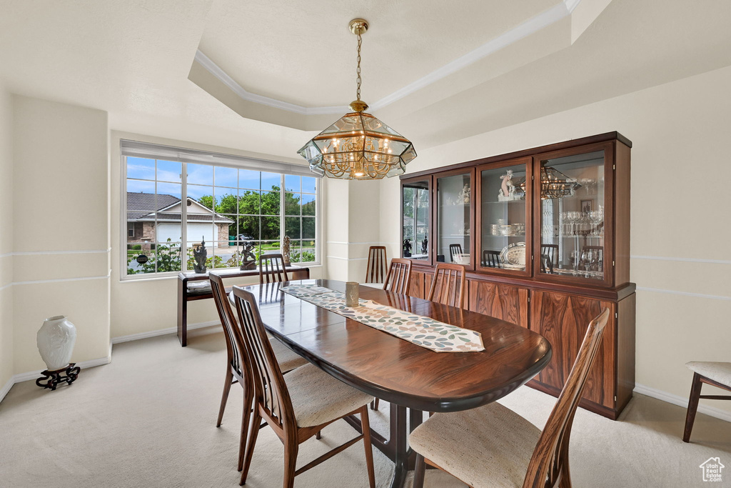 Dining room featuring a tray ceiling, a chandelier, baseboards, and light carpet