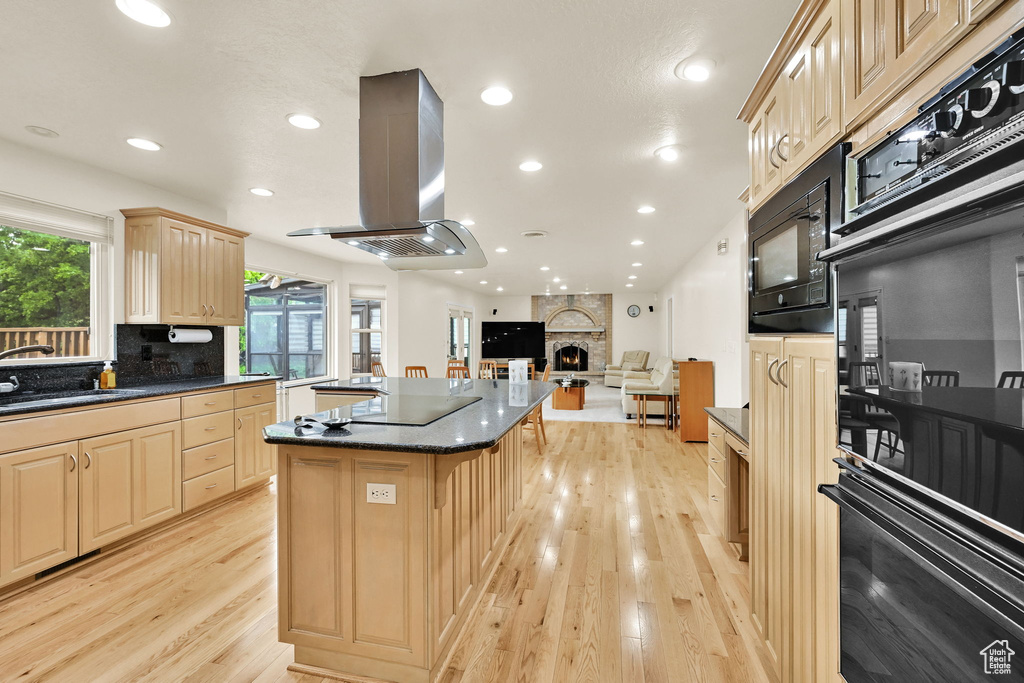 Kitchen with a sink, island exhaust hood, a kitchen island, black appliances, and light wood-style floors