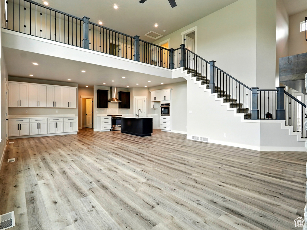 Unfurnished living room with a high ceiling, light wood-type flooring, stairs, a sink, and baseboards