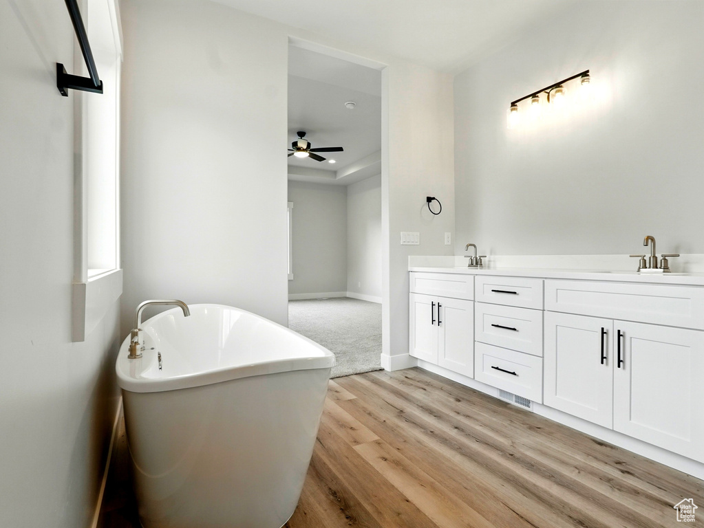 Full bathroom with wood finished floors, a freestanding bath, a ceiling fan, double vanity, and baseboards
