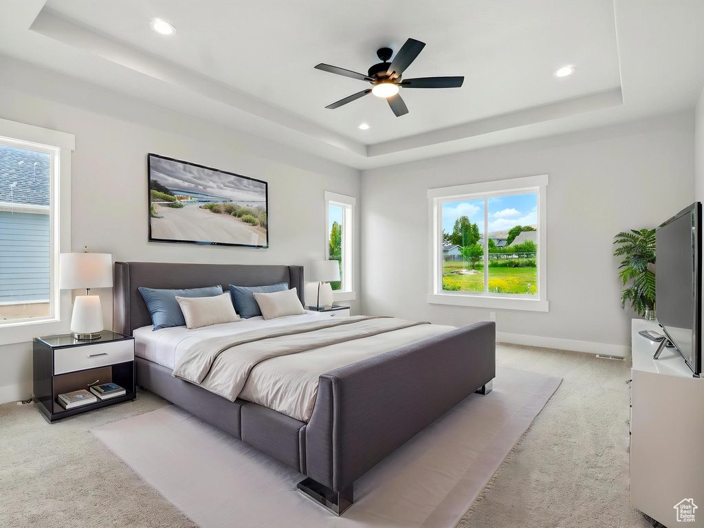 Bedroom with a raised ceiling, light carpet, multiple windows, and recessed lighting