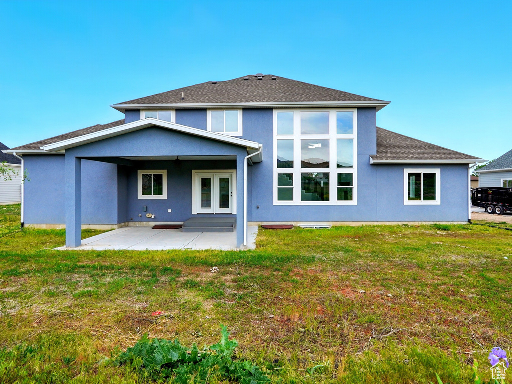 Back of house with a patio, stucco siding, a lawn, and roof with shingles