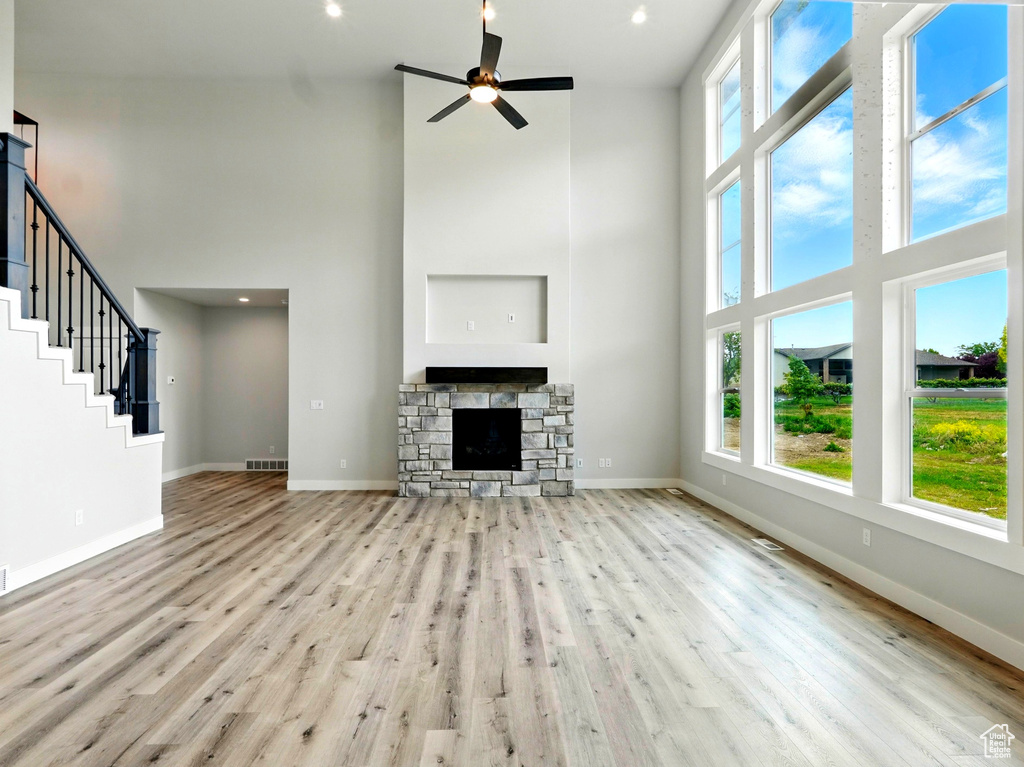 Unfurnished living room with a high ceiling, ceiling fan, wood finished floors, baseboards, and a stone fireplace