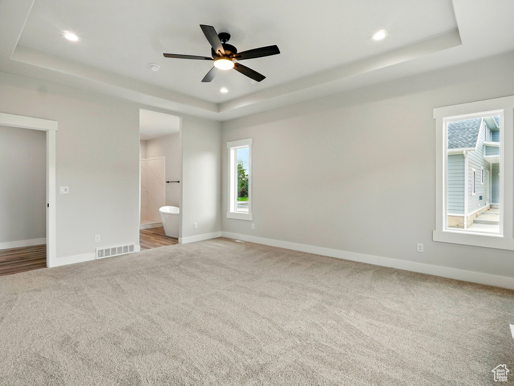 Unfurnished bedroom with a raised ceiling, light carpet, baseboards, recessed lighting, and ensuite bathroom