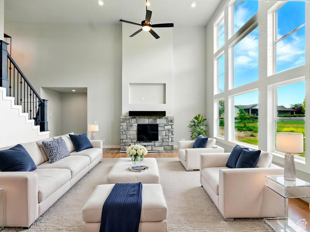 Living room with a high ceiling, ceiling fan, wood finished floors, recessed lighting, and a stone fireplace