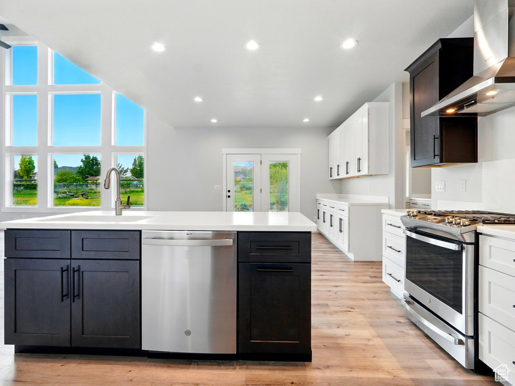 Kitchen featuring appliances with stainless steel finishes, wall chimney range hood, a sink, light countertops, and recessed lighting