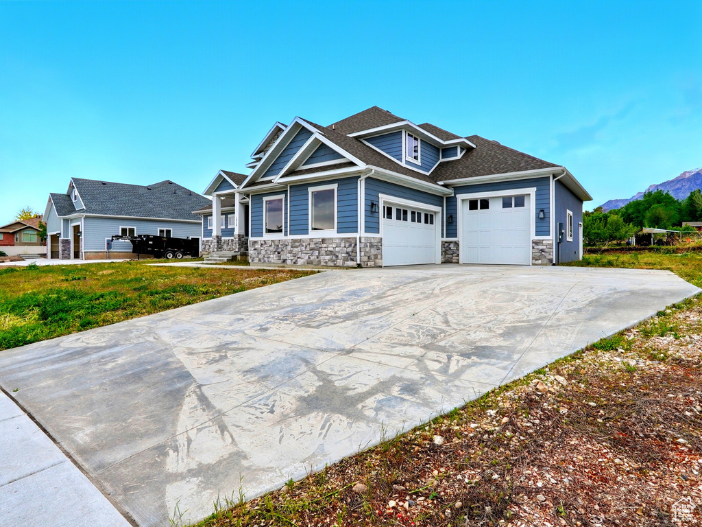 Craftsman house with stone siding, a garage, concrete driveway, and a mountain view