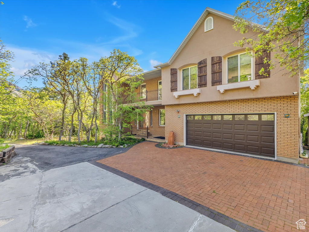 View of front of home featuring decorative driveway, brick siding, an attached garage, and stucco siding