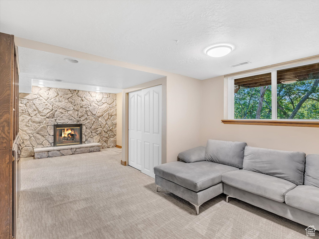 Living room featuring light carpet, a stone fireplace, and a textured ceiling