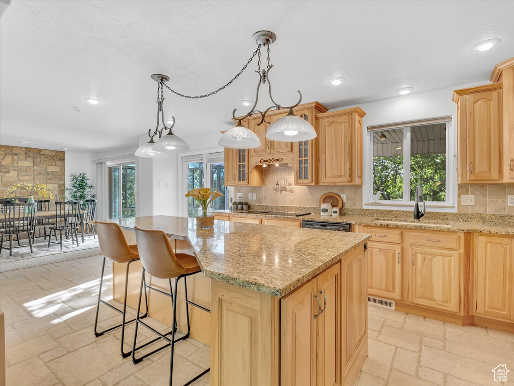 Kitchen with a sink, light brown cabinetry, a center island, decorative backsplash, and light stone counters