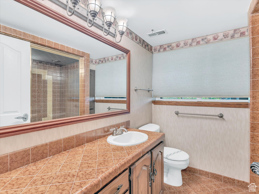 Bathroom with toilet, vanity, a tile shower, tile patterned floors, and wallpapered walls