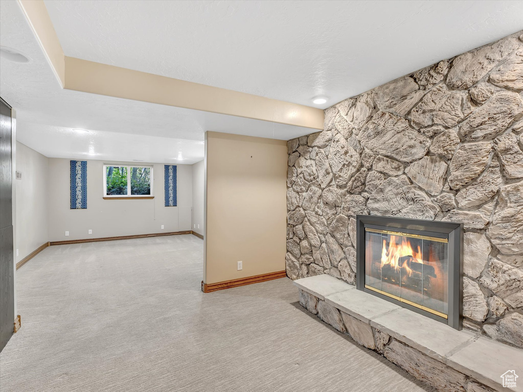Unfurnished living room with carpet flooring, a stone fireplace, and baseboards