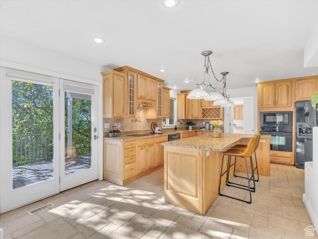 Kitchen featuring black appliances, tasteful backsplash, a kitchen island, glass insert cabinets, and light stone counters