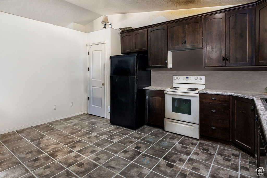 Kitchen featuring freestanding refrigerator, white range with electric stovetop, dark brown cabinets, lofted ceiling, and light countertops