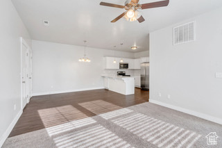Unfurnished living room featuring baseboards, a chandelier, ceiling fan, and dark wood-type flooring