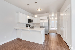 Kitchen featuring stainless steel appliances, a peninsula, light countertops, white cabinetry, and dark wood-style floors