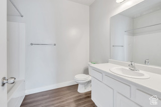 Full bathroom featuring toilet, wood finished floors, vanity, baseboards, and bathing tub / shower combination