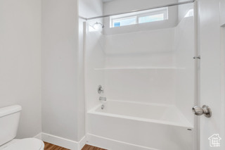 Bathroom with toilet, wood finished floors, baseboards, and shower / bathtub combination