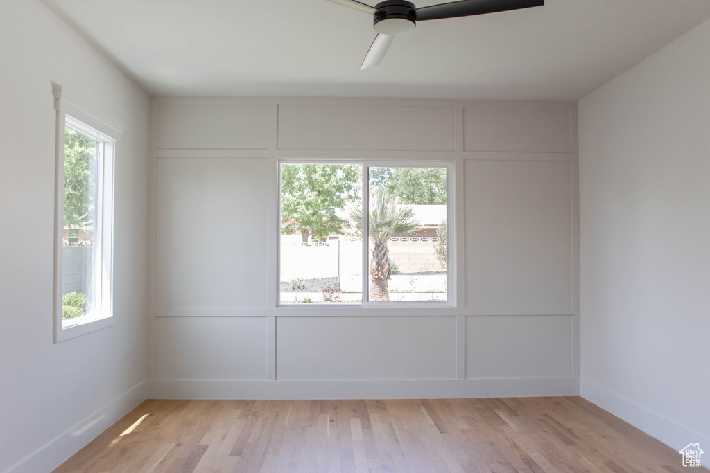 Empty room featuring a decorative wall, a ceiling fan, light wood-style flooring, and baseboards