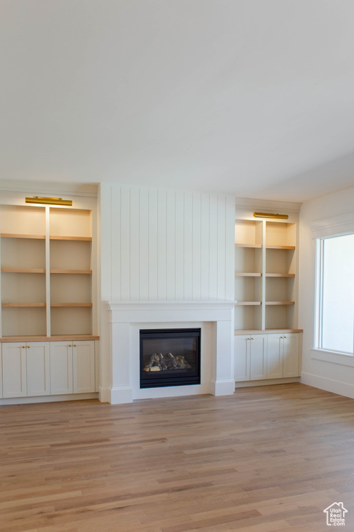 Unfurnished living room with a glass covered fireplace, light wood finished floors, built in features, and baseboards