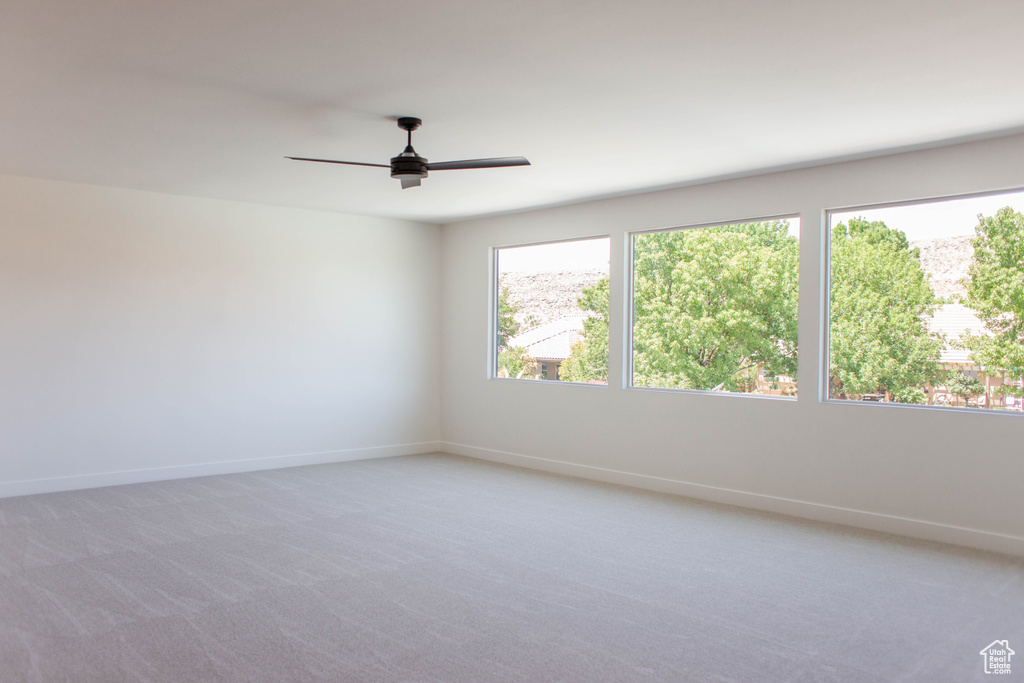 Spare room featuring light colored carpet, baseboards, and ceiling fan