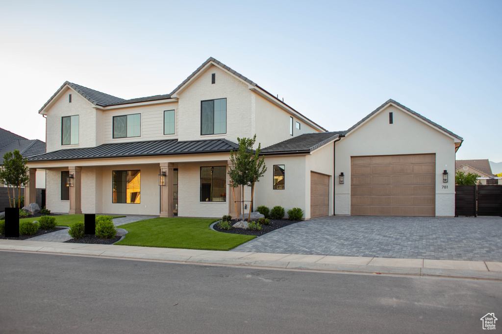 View of front of home with a standing seam roof, an attached garage, driveway, metal roof, and brick siding