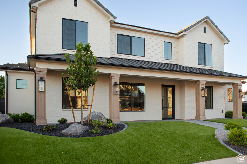 View of front of property featuring a standing seam roof, brick siding, a porch, a front lawn, and metal roof