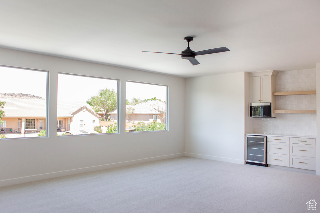 Unfurnished room with beverage cooler, light colored carpet, baseboards, a ceiling fan, and a bar