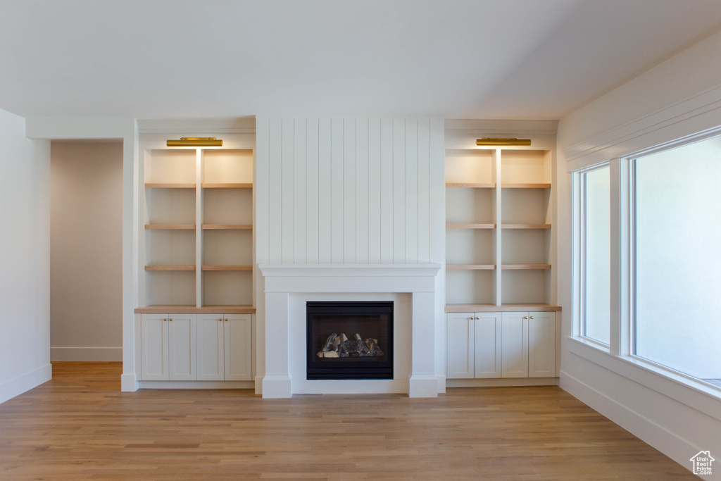Unfurnished living room featuring light wood-style floors, a fireplace, plenty of natural light, and baseboards