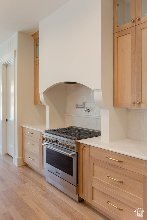 Kitchen with high end stove, light brown cabinets, light wood-type flooring, and backsplash